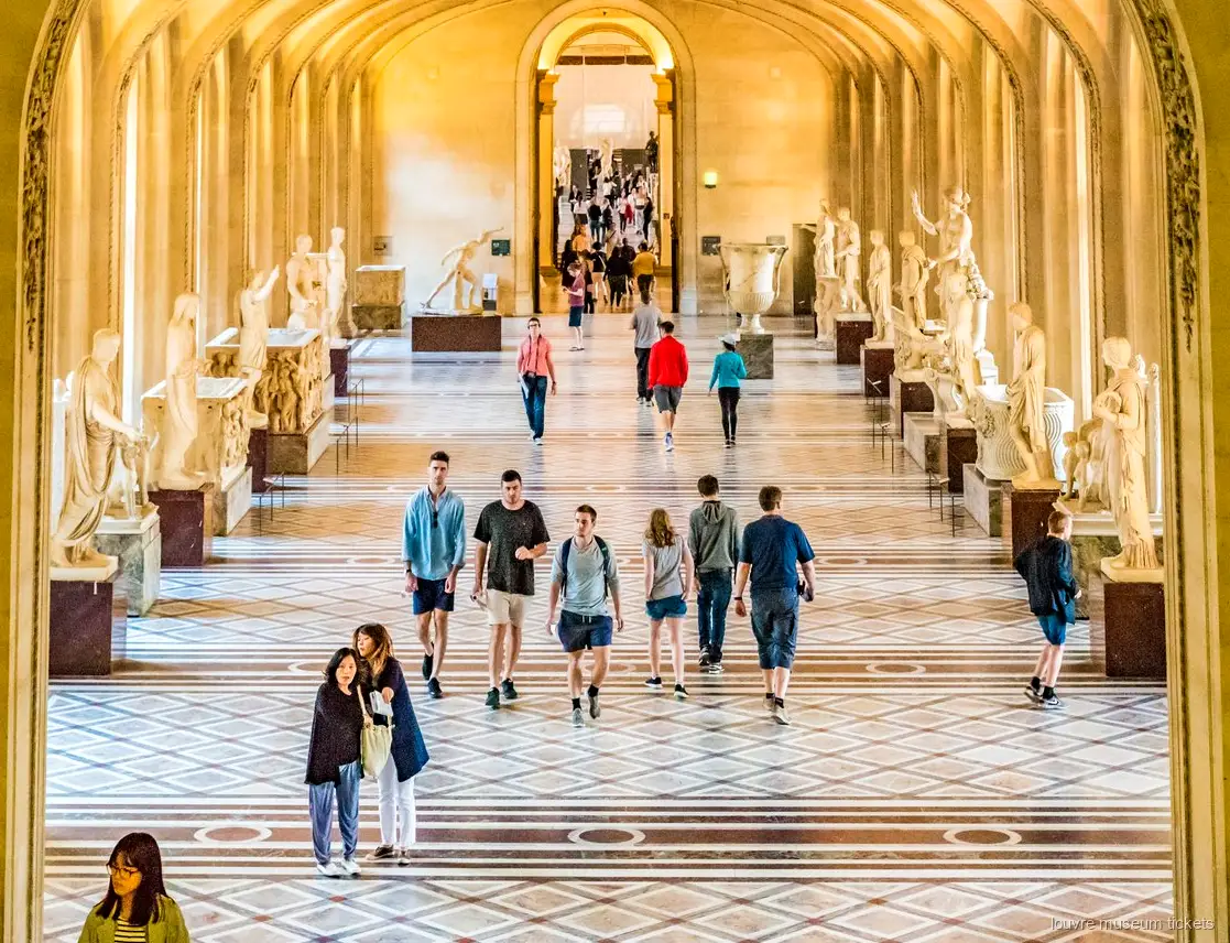 Visitatori in una galleria di sculture classiche con archi e pavimento in marmo, vista con biglietti Museo del Louvre