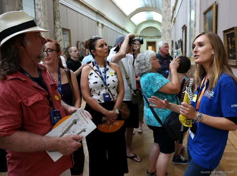 Guide i blå trøje taler til en gruppe med Louvre kort i et malerigalleri, en guidet tur med Louvre billetter