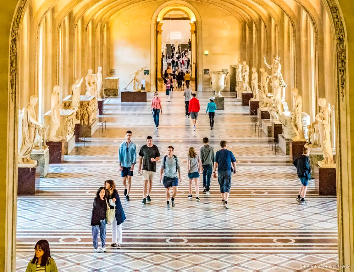 Bezoekers in een galerij met klassieke beelden, bogen en marmeren vloer, gezien met Louvre museum tickets