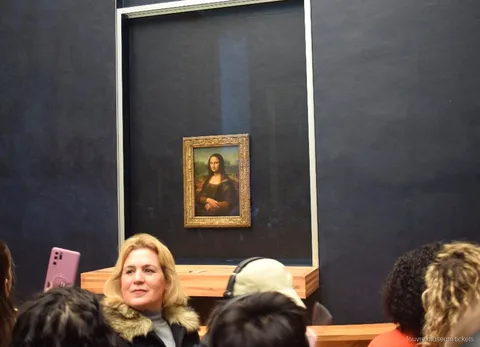 Gæster foran Mona Lisa bag glas på den mørke væg i salen, et højdepunkt på turen med Louvre billetter