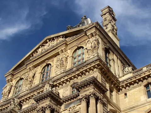 Gebeeldhouwde Louvre gevel met beelden, fronton en zuilen onder een blauwe lucht, gezien met Louvre museum tickets