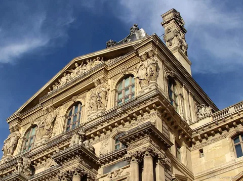 Verzierte Louvre Fassade mit Statuen, Giebel und Säulen vor tiefblauem Himmel, gesehen mit Louvre Tickets