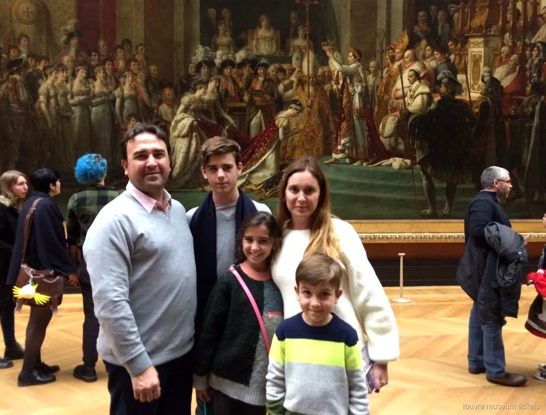 Familia de cinco posando ante La coronación de Napoleón en un tour privado con entradas al Museo del Louvre
