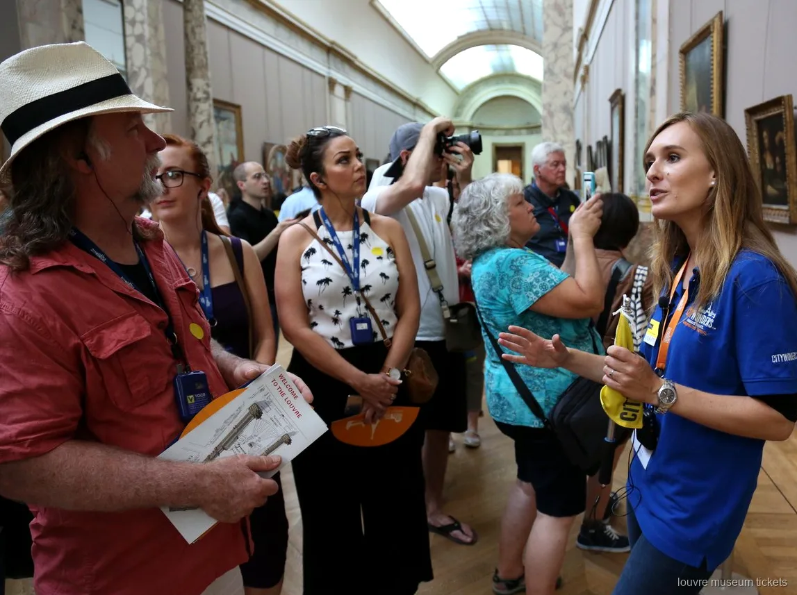 Guia de camisola azul a falar a um grupo com mapas do Louvre numa galeria de pintura, visita com bilhetes Museu do Louvre