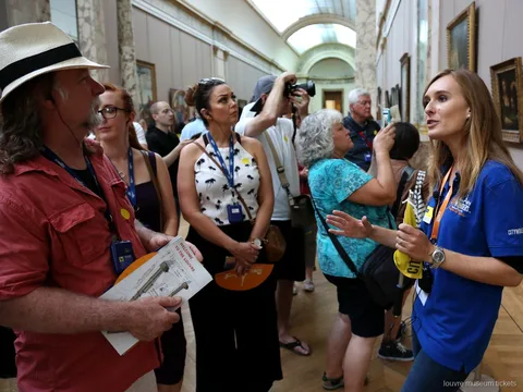 Guide en polo bleu face à un groupe muni de plans du Louvre dans une galerie, visite avec billets musée du Louvre
